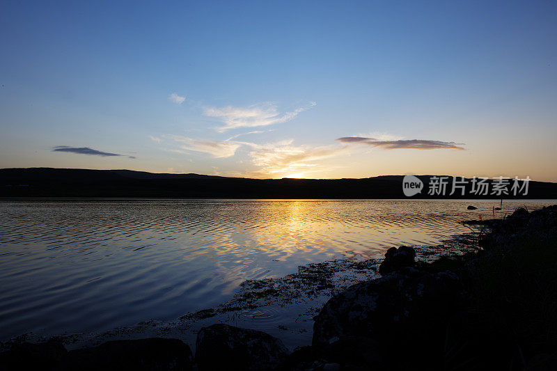 苏格兰斯凯岛(Isle of Skye)的爱丁堡附近的海岸上，格雷肖尼什湖(Loch Greshornish)上的落日天空映衬着山脉的轮廓。